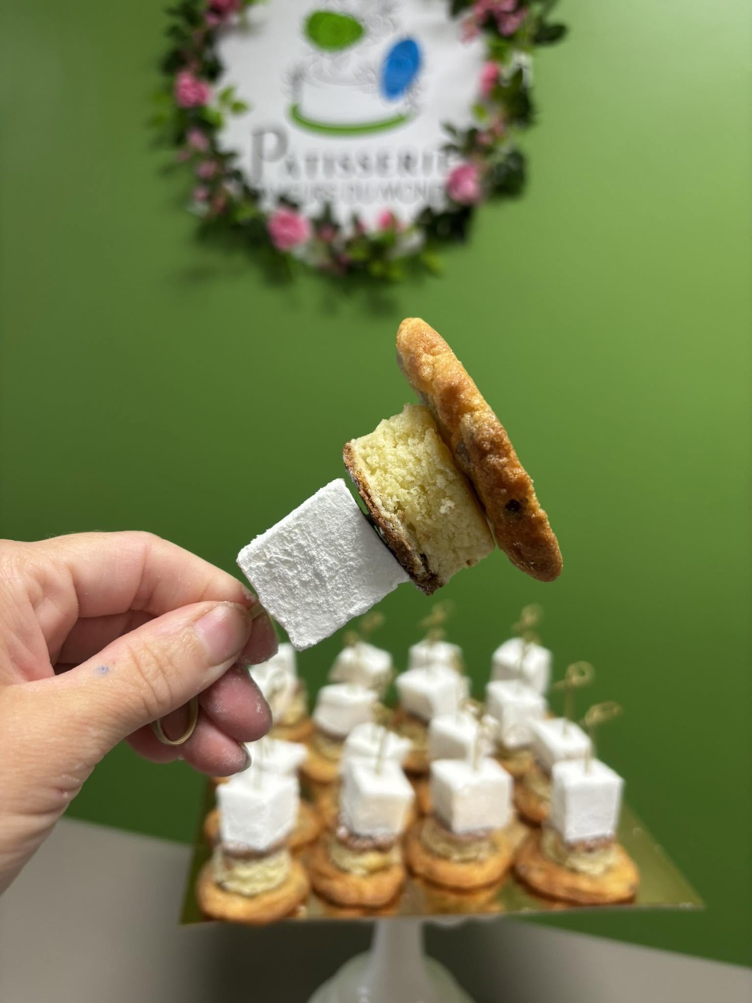 Dessert signature de la Pâtisserie Saveurs du Monde, présenté devant leur enseigne fleurie sur fond vert